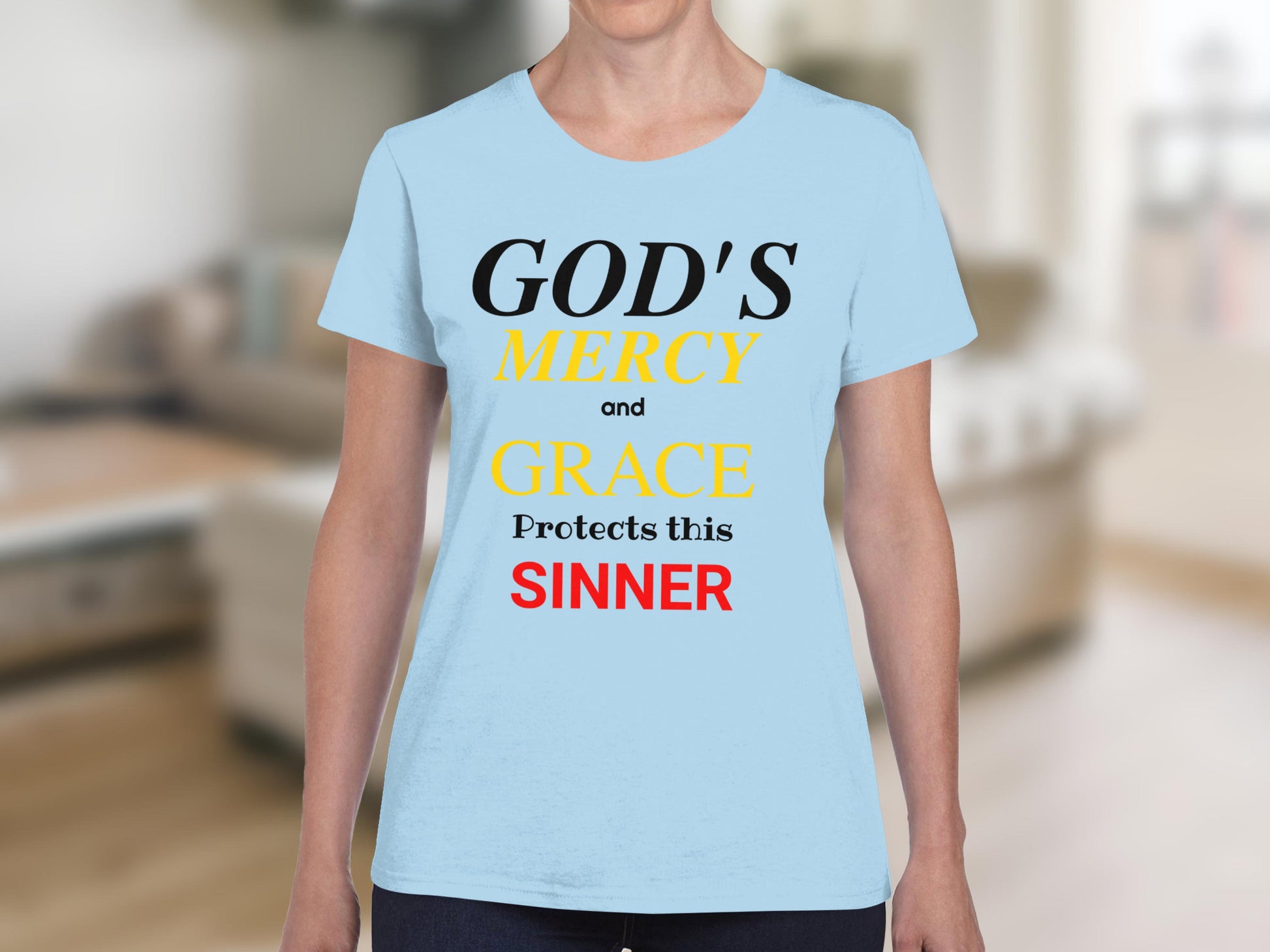 Light blue t-shirt with black, yellow, and red text reading "GOD'S MERCY and GRACE Protects this SINNER".